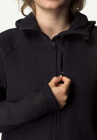 Schwarze Zip-Jacke aus einem strukturierten, atmungsaktiven Stoff mit Kapuze und gerippten Ärmeln, ausgestattet mit einer vorderen Reißverschlusstasche.