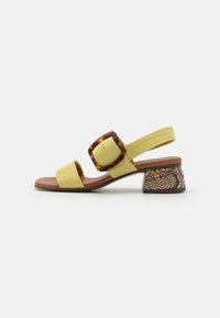 Gul sandal med en bred rem, detalj av skilpadde-mønster på spennen og en teksturert brun blokkhelt som ligner snakeskin.