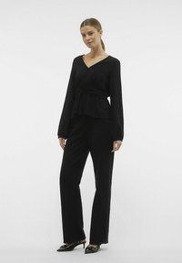 Top nero a maniche lunghe con scollatura a V e vita arricciata, abbinato a pantaloni neri a gamba larga e tacchi a punta neri. Texture del tessuto liscia.