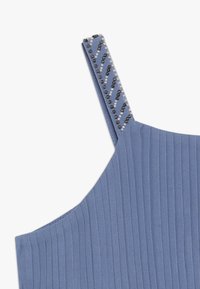 Niebieski prążkowany top z ozdobnym paskiem na ramię, zdobionym czarno-białymi koralikami w zygzakowaty wzór.