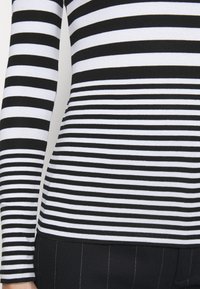 Black and white striped long-sleeve top with a fitted design. The stripes vary in width, with a smooth fabric texture.