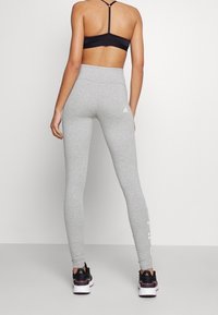 Grå sportleggings i stretchmaterial med hög midja och subtil logotyp på vaden, kombinerade med svarta sportskor.