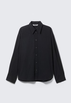 Svartstripet skjorte med knapper, spiss krage, lange ermer og avslappet passform. Har subtile vertikale striper og knappdetaljer.