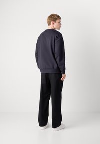 Felpa navy con maniche lunghe e polsini a coste, abbinata a pantaloni neri a gamba larga e sneakers bianche. Design semplice e casual.