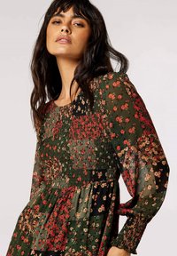 Blumen Kleid mit grünem Grundton, roten und gelben Blumen, durchsichtigen langen Ärmeln, gerafftem Oberteil und schichtiger Rockgestaltung.