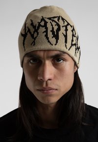 Gorro de punto en beige con patrones abstractos en negro, que presenta un ajuste ceñido y una textura suave. Camiseta de tela negra debajo.