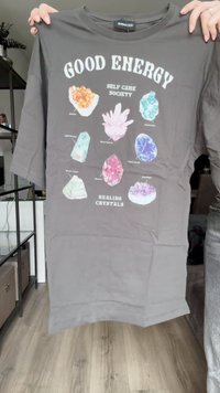 Šedé tričko s rôznymi farebnými grafikami kryštálov a textom. Uvoľnený strih s krátkymi rukávmi; dizajn obsahuje označenia pre každý kryštál.