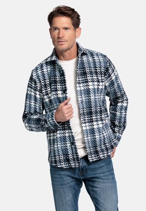 Geruite jas in blauwe, zwarte en witte tinten; gemaakt van zacht materiaal met lange mouwen, knopen aan de voorkant en een ontspannen pasvorm. Draagt over een wit shirt.