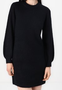 Robe pull noire en tricot avec un col ras du cou, des manches longues et une coupe décontractée, comportant des poignets et un ourlet côtelés pour plus de texture.