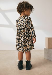 Leopardprint kjole med lange ærmer, samlet nederdel og bølget kant. Sorte combat boots med snøretrim. Baggrunden har neutrale farver.