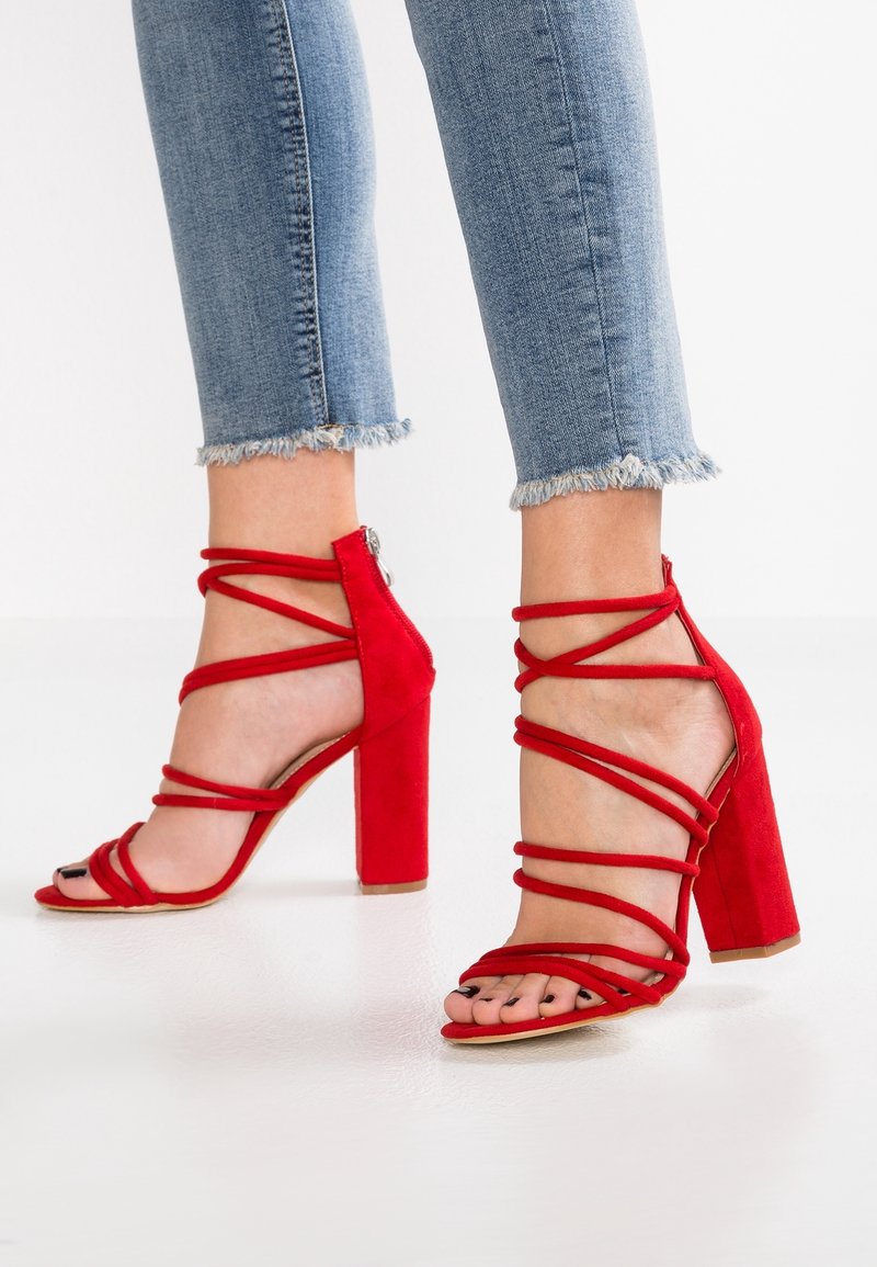 Sandales à talons hauts en daim rouge avec un talon bloc et plusieurs lanières entrecroisées. Design à bout ouvert avec une finition texturée.