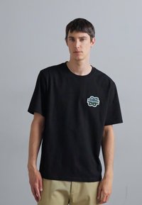 Black short-sleeve t-shirt made from cotton, featuring a small green graphic logo on the left chest and a relaxed fit.