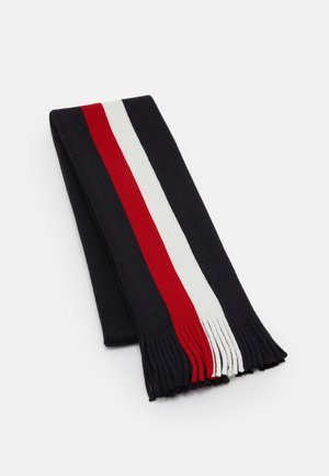 Bufanda de punto con base negra y rayas verticales rojas y blancas, con textura acanalada y flecos en los extremos, extendida sobre una superficie blanca.