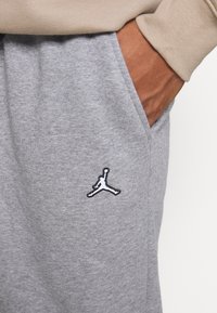 Grå mjukisbyxor gjorda av ett mjukt, ventilerande material. Har en svart och vit broderad Jumpman-logga på vänster sida.