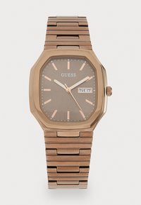 Rosa gull oktagonal klokke med brun urskive, sølvtime markører, datovisning og metallarmbånd. Reflekterende glatt finish på kassen og båndet.
