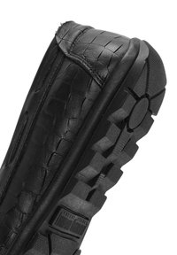 Schwarzer Lederschuh mit strukturiertem Obermaterial, das ein Reptilmuster aufweist. Dicke Gummisohle mit Profil und kreisförmigem Akzent.