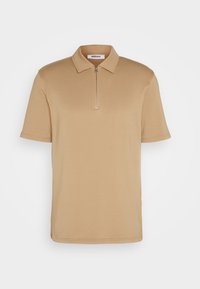 Polo beige à manches courtes, avec col et détail à zip quart. Fabriqué en tissu lisse sans motifs ni accents visibles.