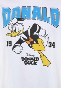 Fehér pamut póló, Donald Duck grafikájával, aki fekete öltönyt és csokornyakkendőt visel, miközben fut, kék feliratokkal felül és alul.