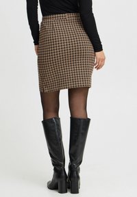 Rjava krila v vzorcu houndstooth z oprijetim krojem, v kombinaciji z črnimi škornji do kolen. Gladka tekstura in dolžina nad kolenom.