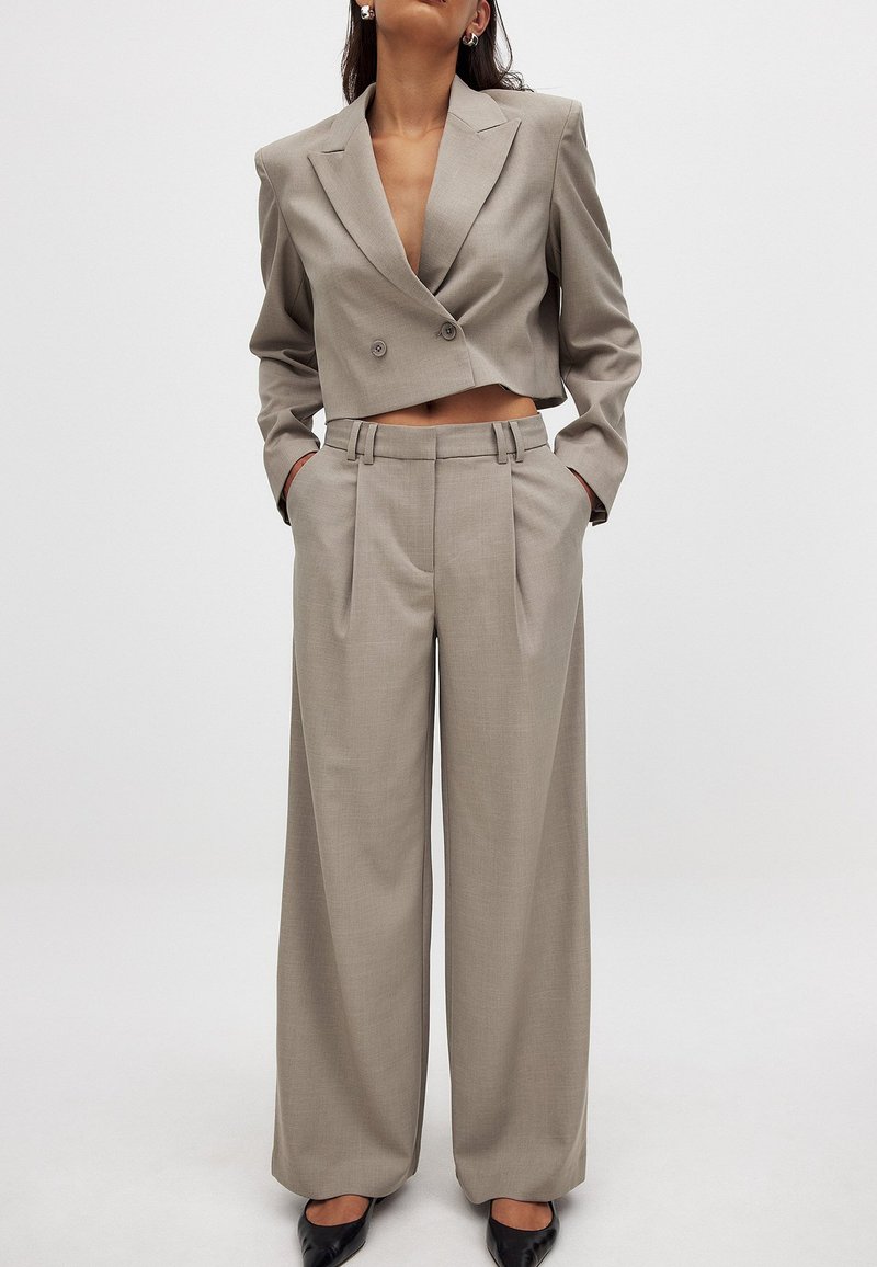 Heled helehall lühikese joonega bleiser kahekordsete nuppudega ja laiad püksid, millel on sile eesmine osa, küljetaskud ja sile kangastekstuuri.