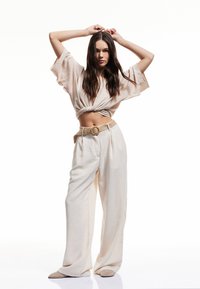 Lichtbeige cropped top met een geknoopte voorkant, gecombineerd met hoge taille, wijde crèmekleurige broek en een geweven riem met een ronde sluiting.
