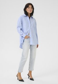 Cămașă cu dungi albastre deschise,button-up, cu un croi lejer, mâneci lungi și un tiv curbat, asortată cu blugi deschiși la culoare și pantofi cu toc negri.