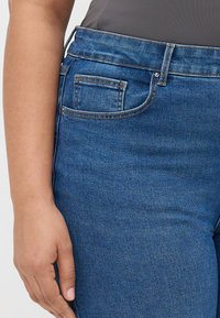 Modre denim hlače z značilnim pet-pocket dizajnom, vsestranskim srednje visokim pasom in subtilnim zbledelostjo, ki prikazuje gladko teksturo.