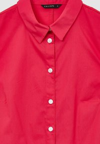 Camicia rossa con bottoni, dotata di colletto, caratterizzata da bottoni bianchi e un tessuto leggero e liscio. Etichetta delle taglie visibile. Design semplice, senza fantasie.