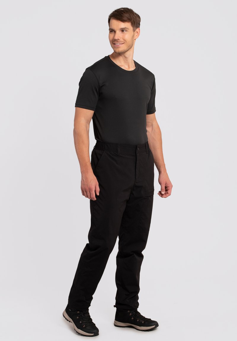 Czarna koszulka z krótkim rękawem w połączeniu z czarnymi spodniami, charakteryzującymi się luźnym krojem i elastycznym paskiem, noszona z czarnymi butami trekkingowymi.