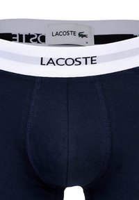 Marineblaue Baumwoll-Boxershorts mit einem weißen elastischen Bund, der das Lacoste-Logo trägt, für Komfort und Halt entworfen.