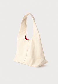 Bežová textilná taška s širokým popruhom a jemným červeným vnútorným podšívaním, stojaca vzpriamene na bielom pozadí.