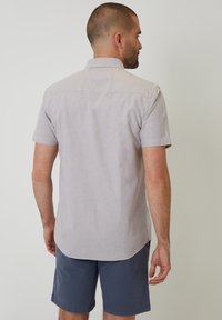 Camisa de manga corta, de color gris claro, en una tela suave, con un cuello abotonado y un dobladillo recto, combinada con pantalones cortos de color marino.