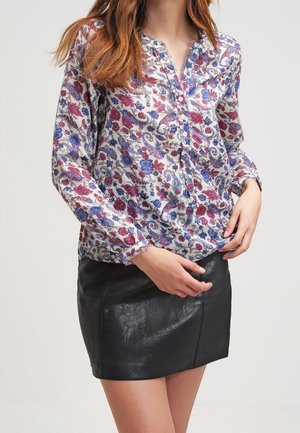Blusa a maniche lunghe con bottoni e motivo floreale in rosso, blu e bianco su uno sfondo trasparente; abbinata a una gonna in pelle nera.