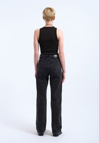 Black tank top paired with high-waisted, straight-leg jeans. The jeans feature a faded wash and traditional back pockets.