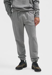 Graue Jogginghose mit einem elastischen Bund und Kordelzug sowie gerippten Bündchen. Kleiner Schriftzug "HALO 196819" auf dem linken Bein.