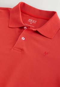 Polo rouge de taille moyenne avec col, deux boutons blancs et logo brodé subtil sur la poitrine, étiquette "Next Regular Fit".