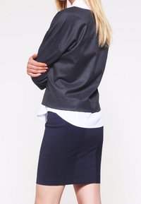 Maglione a maniche lunghe grigio scuro sopra una camicia bianca con colletto, abbinato a una gonna attillata blu navy, che mostra texture lisce e un design a strati.