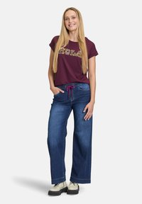 Bordeauxkleurig T-shirt met korte mouwen en een bloemenprint, gecombineerd met donkerblauwe wijde spijkerbroek en lichtgekleurde chunky laarzen. Prominente drawstring bij de taille.