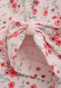 Roze stof met een bloemenpatroon waarin rode en navy bloemen zijn verwerkt, aangevuld met groene bladeren; inclusief een knoopdetail voor het ontwerp.