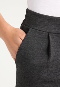 Pantaloni in tessuto grigio e strutturato con vita aderente, tasche laterali e dettagli plissettati vicino alla vita per un tocco di design in più.