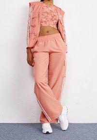 Persikkainen urheiluasu, jossa on lyhyt toppi, jossa on sitruunakuosis, sekä yhteensopivat leveälahkeiset housut, joissa on sivutaskut ja valkoiset raidat.