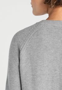 Hellgrauer, gerippter Pullover mit rundem Ausschnitt und Raglanärmeln. Die Textur ist weich und hat eine dezente Dehnbarkeit.