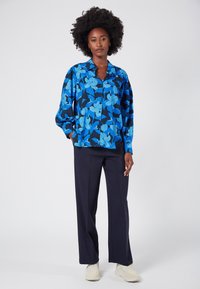 Niebieska koszula z kwiatowym wzorem, zapinana na guziki, wykonana z miękkiego materiału, zestawiona z ciemnoniebieskimi spodniami i jasnymi trampkami.