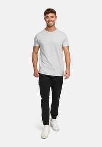 Graues Kurzarm-T-Shirt kombiniert mit schwarzen Cargo-Hosen und weißen Sneakern. Das Modell steht vor einem schlichten weißen Hintergrund.
