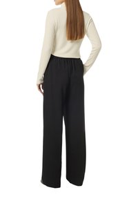 Schwarze weite Hose mit elastischem Bund, kombiniert mit einem cremefarbenen, gerippten Langarmoberteil, das eine glatte Textur und eine figurbetonte Passform zeigt.