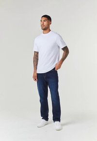 Λευκό βαμβακερό μπλουζάκι με κοντά μανίκια, σε συνδυασμό με σκούρα μπλε τζιν και λευκά αθλητικά παπούτσια. Απλός σχεδιασμός, χαλαρή εφαρμογή και χωρίς ορατά σχέδια.