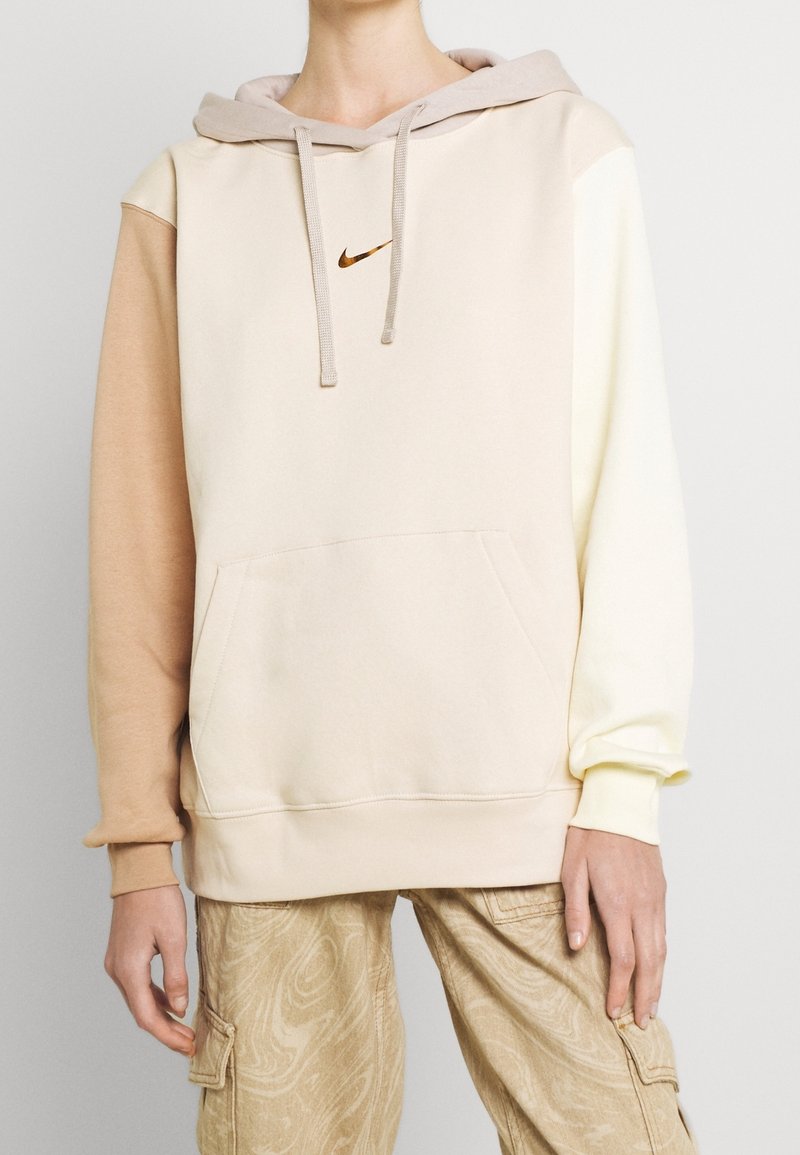 Beige och pastellfärgad hoodie i mjukt tyg, med kenguruficka, dragsko i huvan och liten Nike-logga på bröstet.