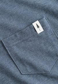 Grafietkleurig katoenen shirt met een linker borstzak met een wit label en een zwarte boomafbeelding. Zachte textuur met gestikte randen.