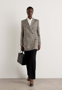 Grau-beige karierte, doppelte Damenblazer mit schwarzen Hosen und einer schwarzen Handtasche kombiniert. Glatter Stoff mit strukturierter Passform.