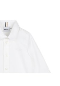 Camisa branca de algodão com parte da frente com botões, gola pontiaguda e logótipo discreto 'BOSS' bordado. Apresenta detalhe ao contrário às riscas na gola.